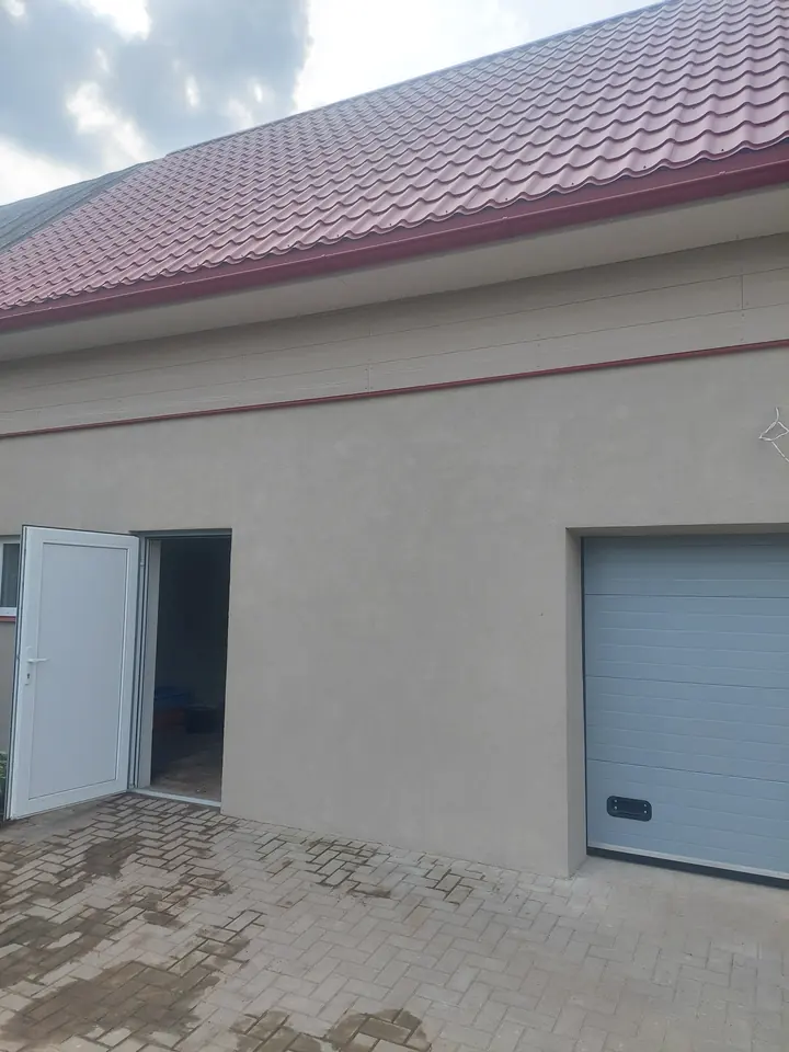 Apmesta mājas fasāde ar garāžas vārtiem un sarkanu jumtu.