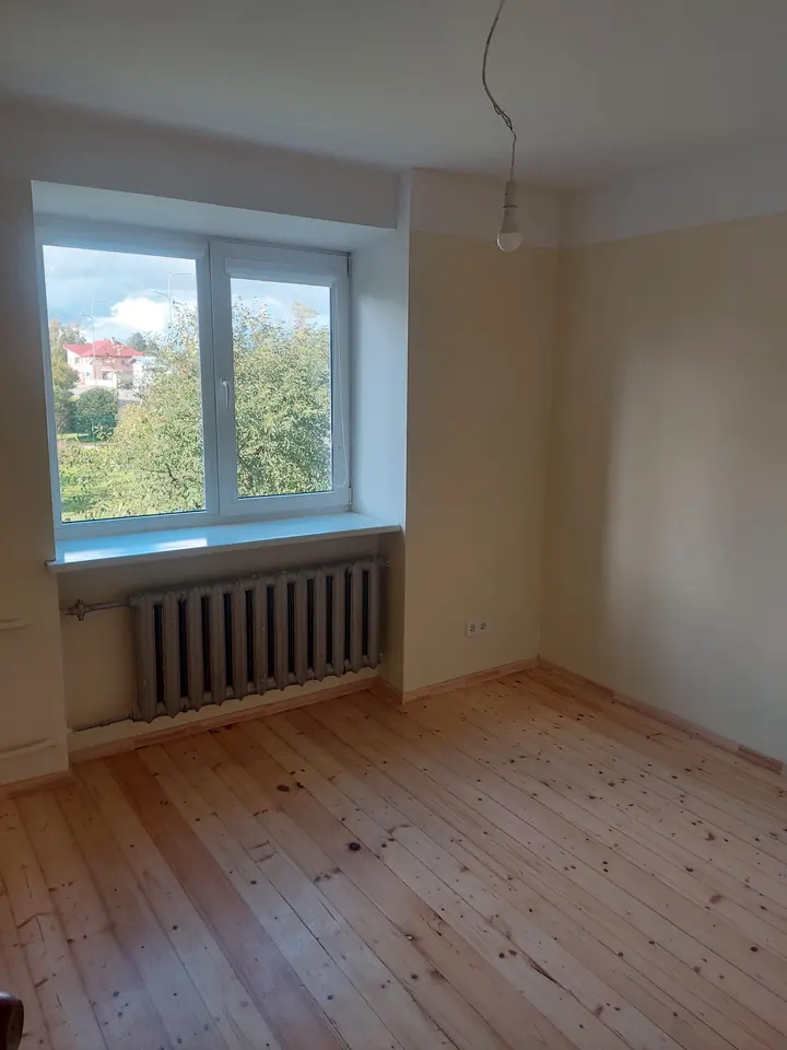 Istaba ar gaišām sienām, logu un koka grīdu.