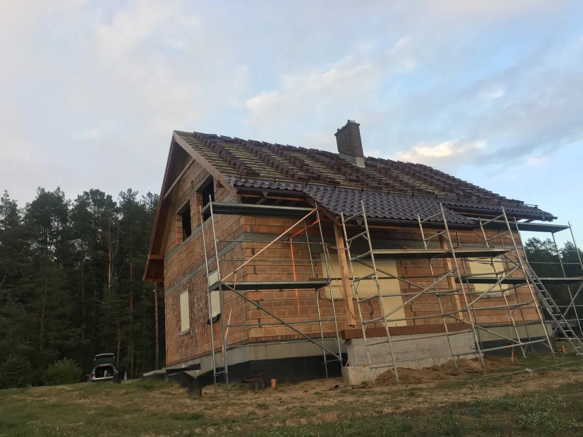 Mūrinis namas su nauju stogu ir pastoliais fasado darbams