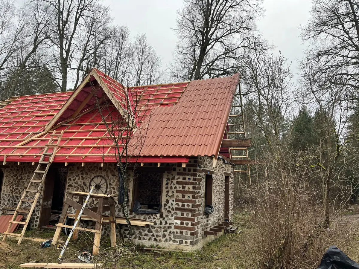 Beveik uždengtas raudonas stogas su frontonu ir kopėčiomis