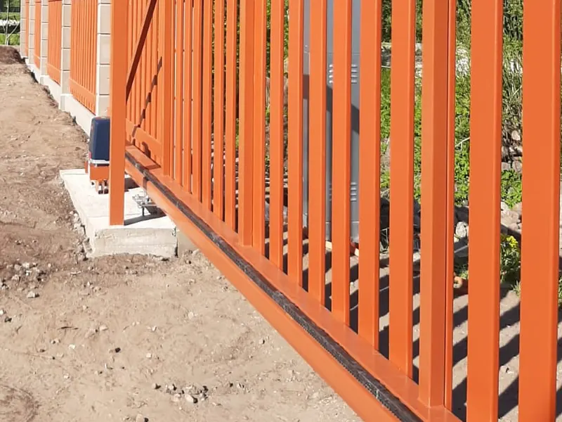 Oranži bīdāmie vārti ar vertikālām līstēm, piedziņu, signāllampu un tāda paša stila žogu