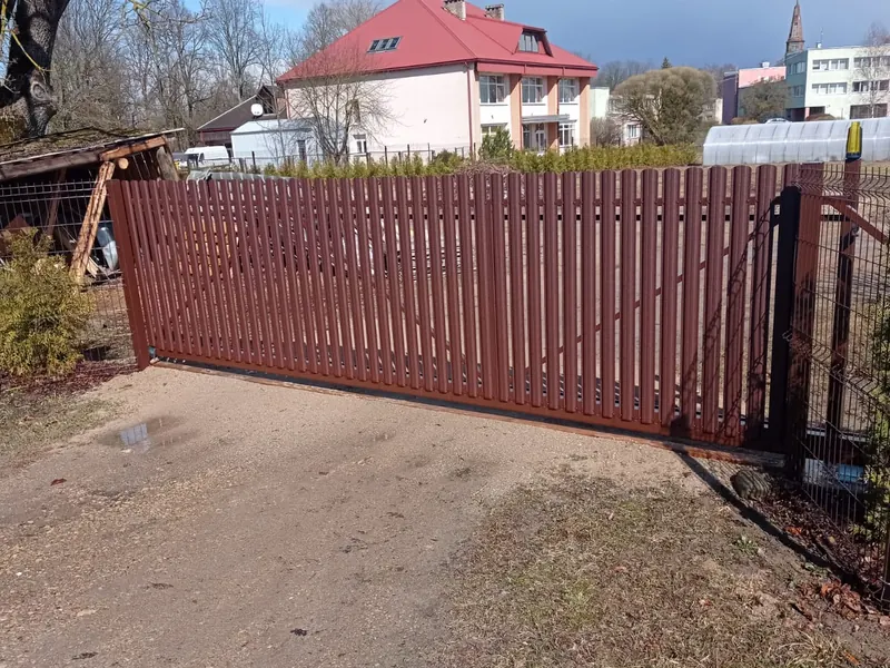 Sarkanbrūni bīdāmie vārti no vertikāla štaketa ar signāllampu, abās pusēs sieta žogs