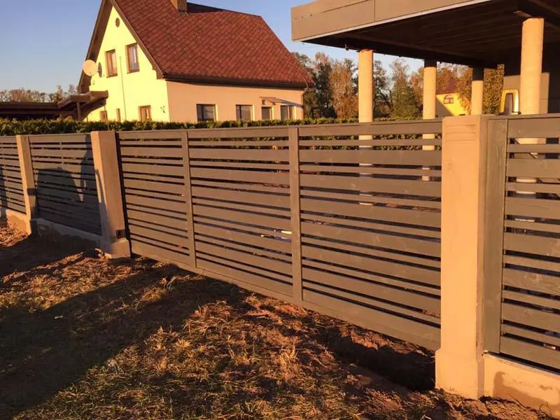 Pelēks žogs no horizontālām lamelēm ar gaišiem stabiem un cokolu